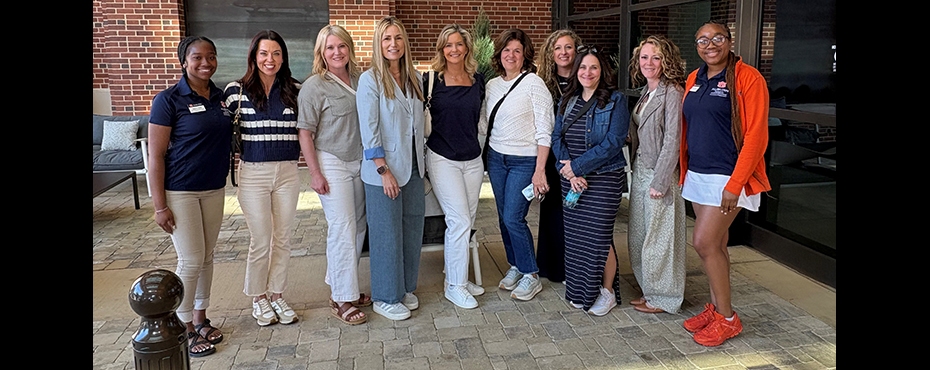 2 female student leaders stand for a picture with 8 female guests in a valet outdoor setting