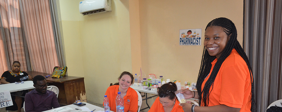 Student standing and two teachers sitting down at a table prepare medications