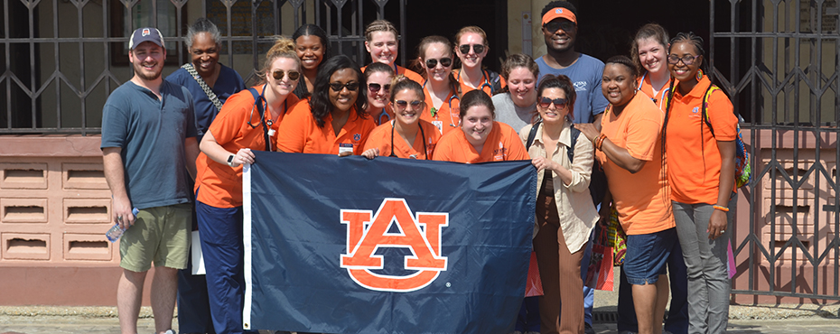 Group of adults standing outside a health clinic holding an AU flag