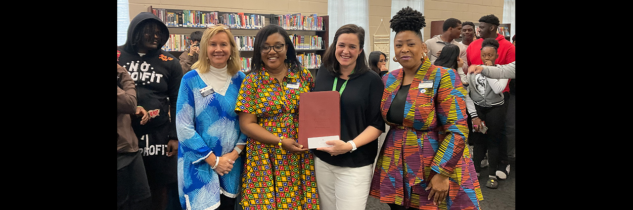 Four women standing in a library holding a binder