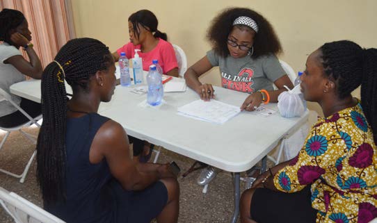 Woman sits at table filling out paperwork surrounded by other women.