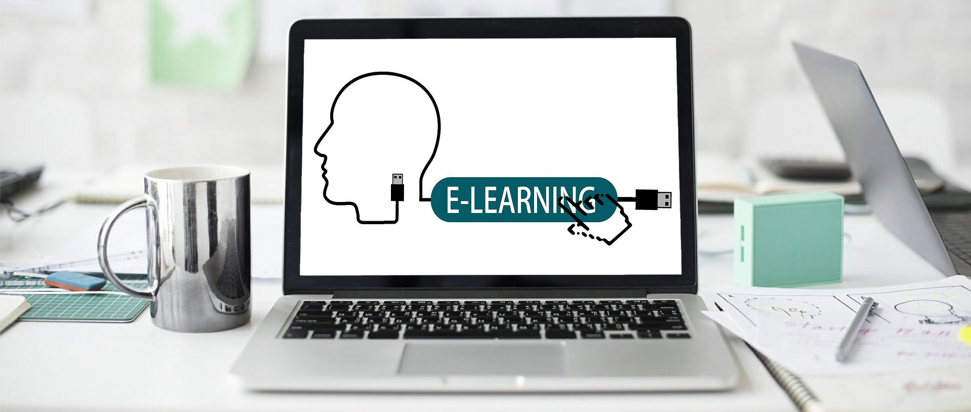 Computer with words E-Learning on screen with coffee cup and notebooks on desk